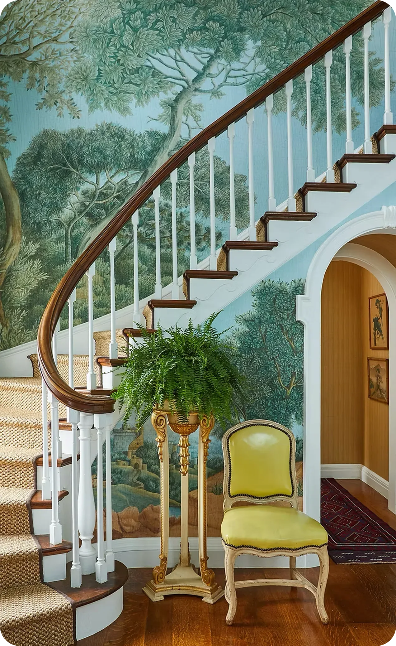 Staircase with a mural of trees and a yellow chair in a room.