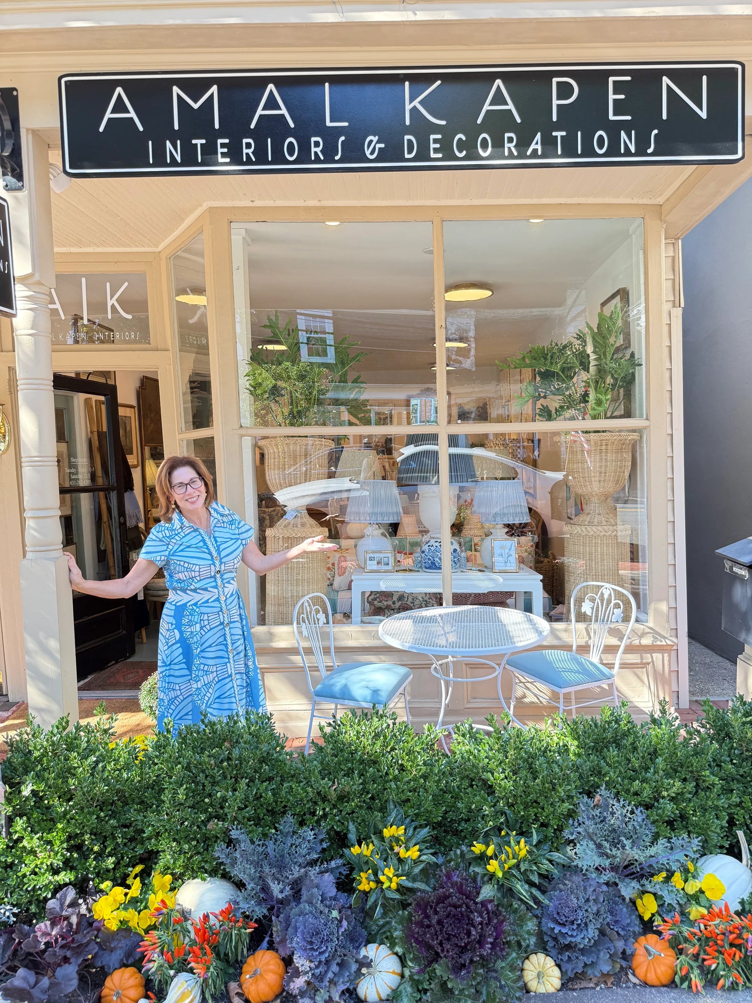 Woman standing outside a store named 'Amalka Pen Interiors & Decorations' with floral decorations.
